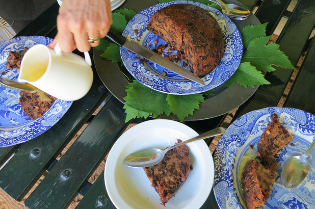 A Christmas plum pudding cut up, slices on plates and half eaten with plum pudding sauce being poured on. 