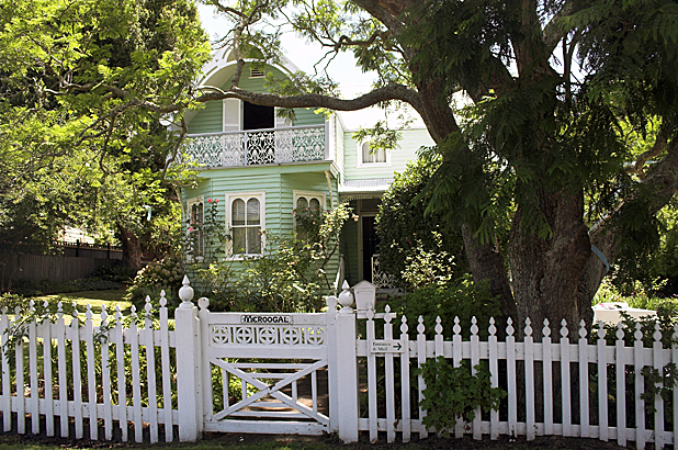 The house seen from the front, behind a white picket fence and gate with Meroogal painted on it.