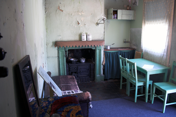 Fireplace, small kitchen area and green table and chairs placed in front of window.