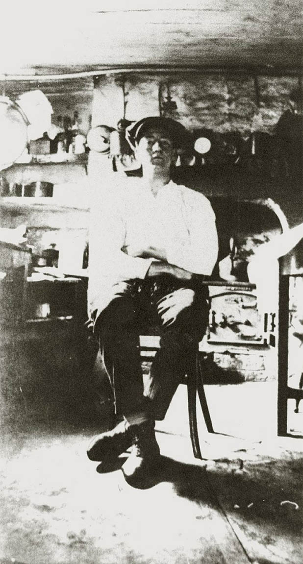 Photograph showing Fred Hughes sitting in the basement kitchen, stove in the background.