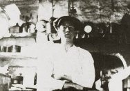 Detail of photograph showing Fred Hughes sitting in the basement kitchen, stove in the background.