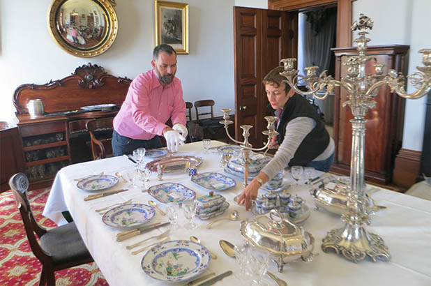 The Cook and the Curator set a table with china and silverware.