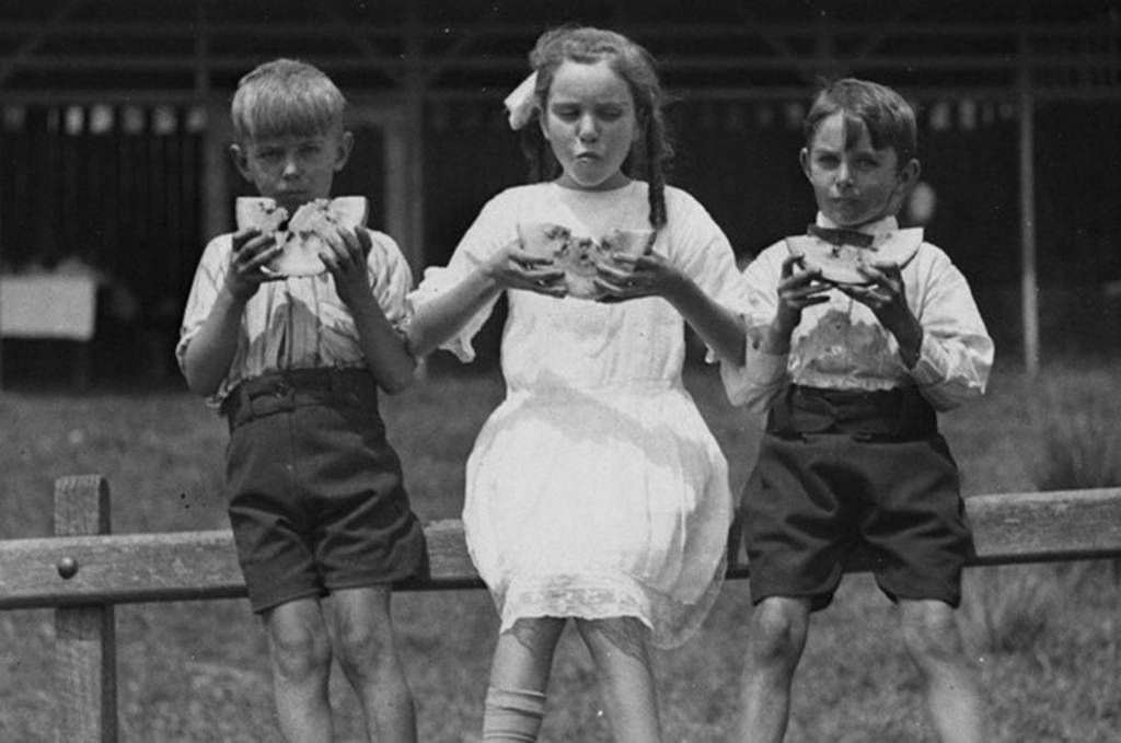 Black and white photograph of three children eating watermelon